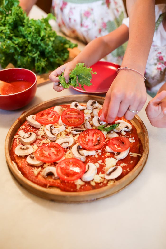 Children and adults preparing a healthy homemade pizza with fresh toppings in the kitchen.